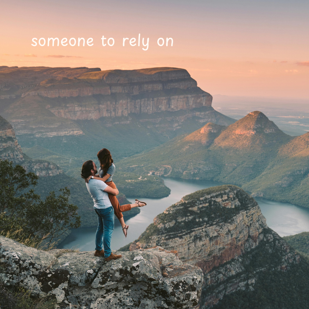 A man and woman are standing with a large ravine in the background. The man is holding the woman up in a romantic position. There is white text that says, "Someone to rely on". 
