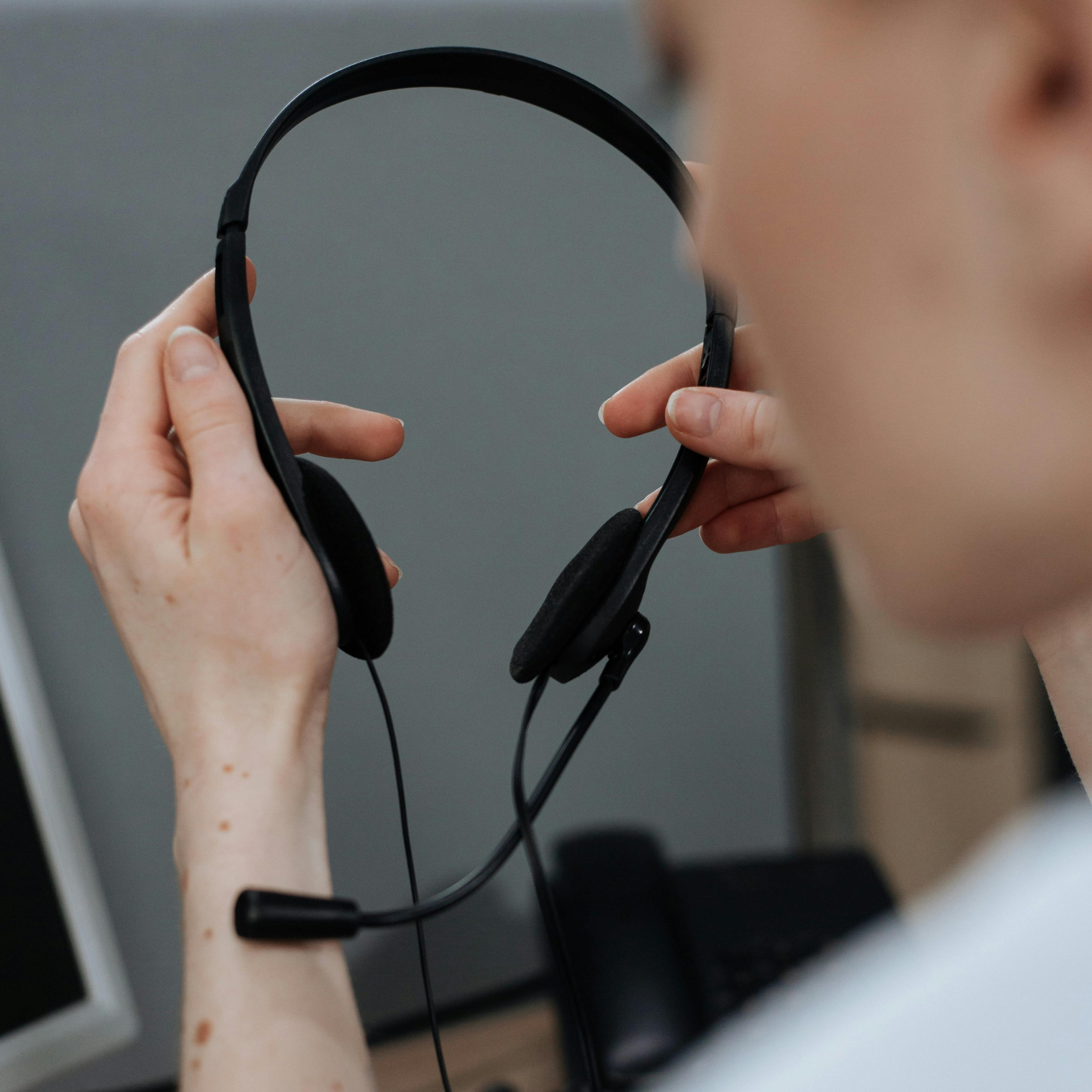 Looking over the shoulder of someone, we see them holding headphones in a motion that indicates they are pputting them on.