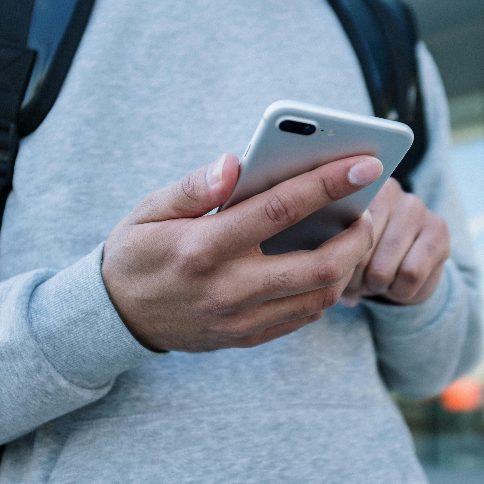 The hands of someone wearing a grey sweater is holding a smartphone which faces away from our view. They are using the smartphone. 